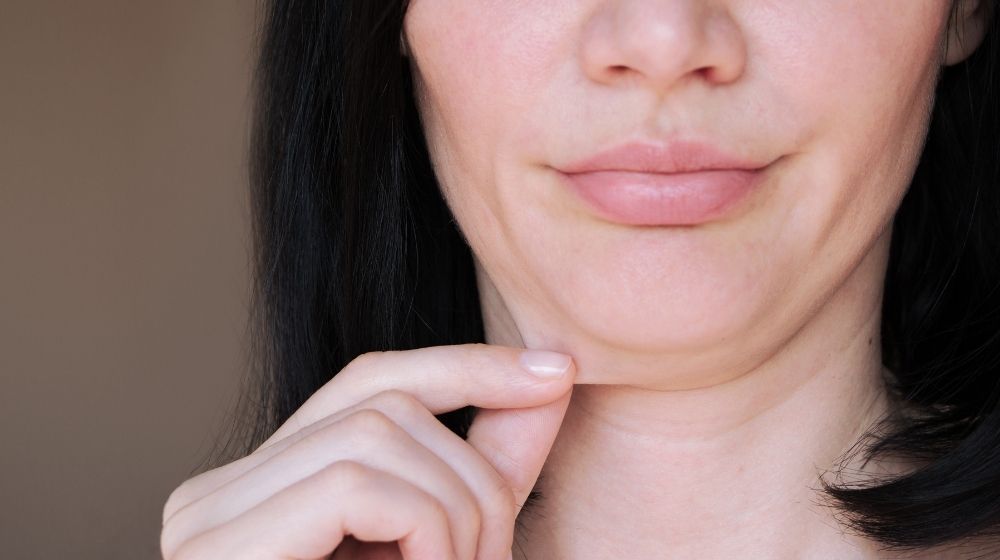a woman is peeling her chin skin | Feature | 7 Different Saggy Skin Solutions