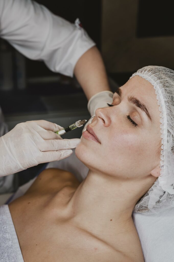 Close-up of a woman's face receiving a dermal filler injection in the cheek from a gloved professional, highlighting the treatment area on the cheek.